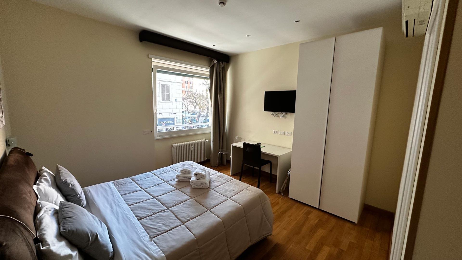 Camera moderna con letto, scrivania, TV e finestra luminosa.