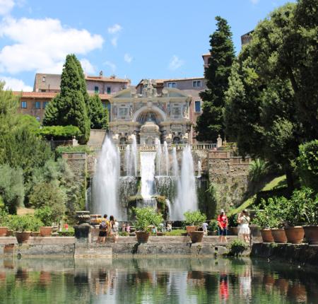Fontana monumentale con cascate in un giardino storico, circondata da alberi e piante.