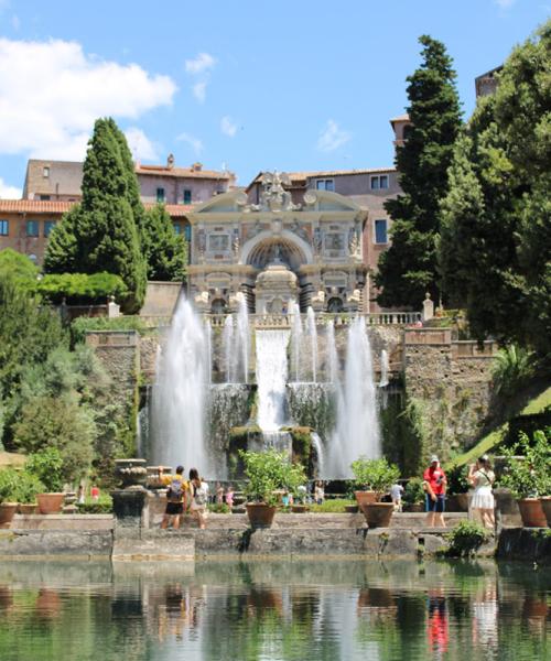 Fontana monumentale con cascate in un giardino storico, circondata da alberi e piante.