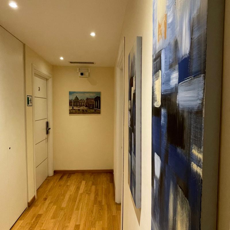 Corridoio con pavimento in legno, quadri astratti e porta bianca.