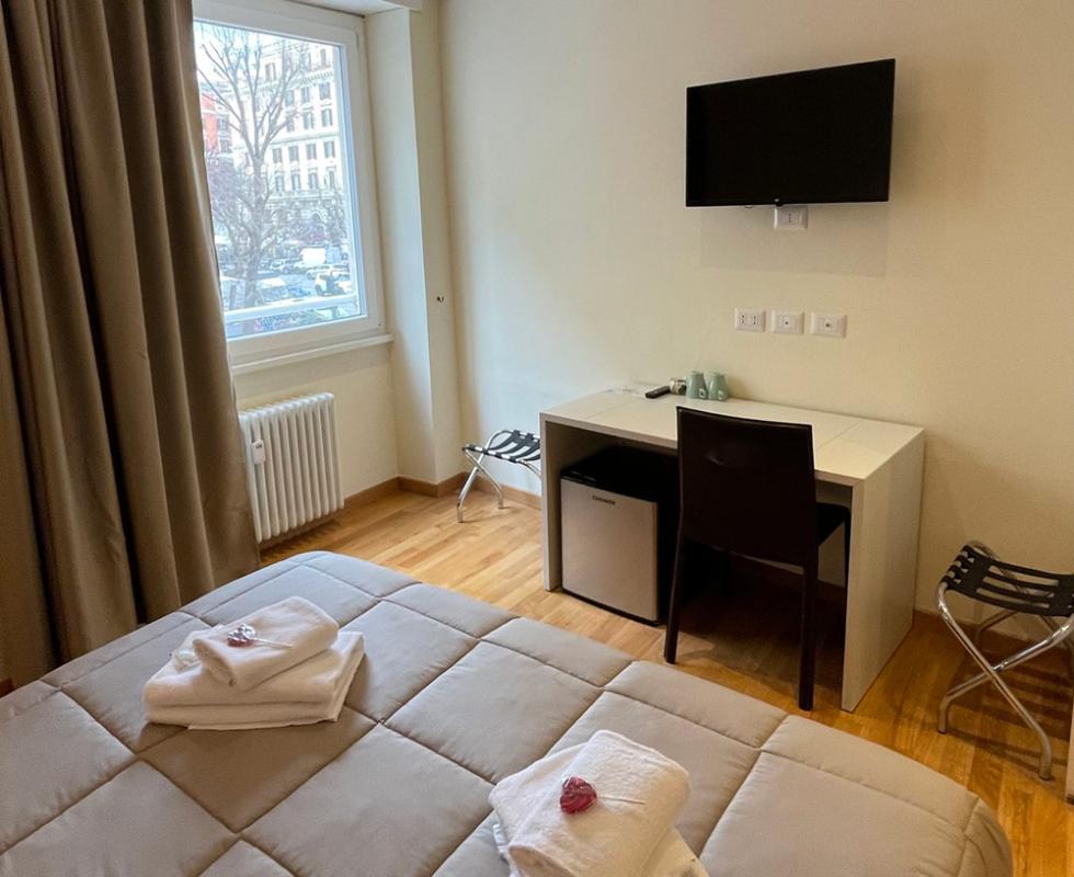 Camera moderna con letto matrimoniale, TV, scrivania e finestra luminosa.