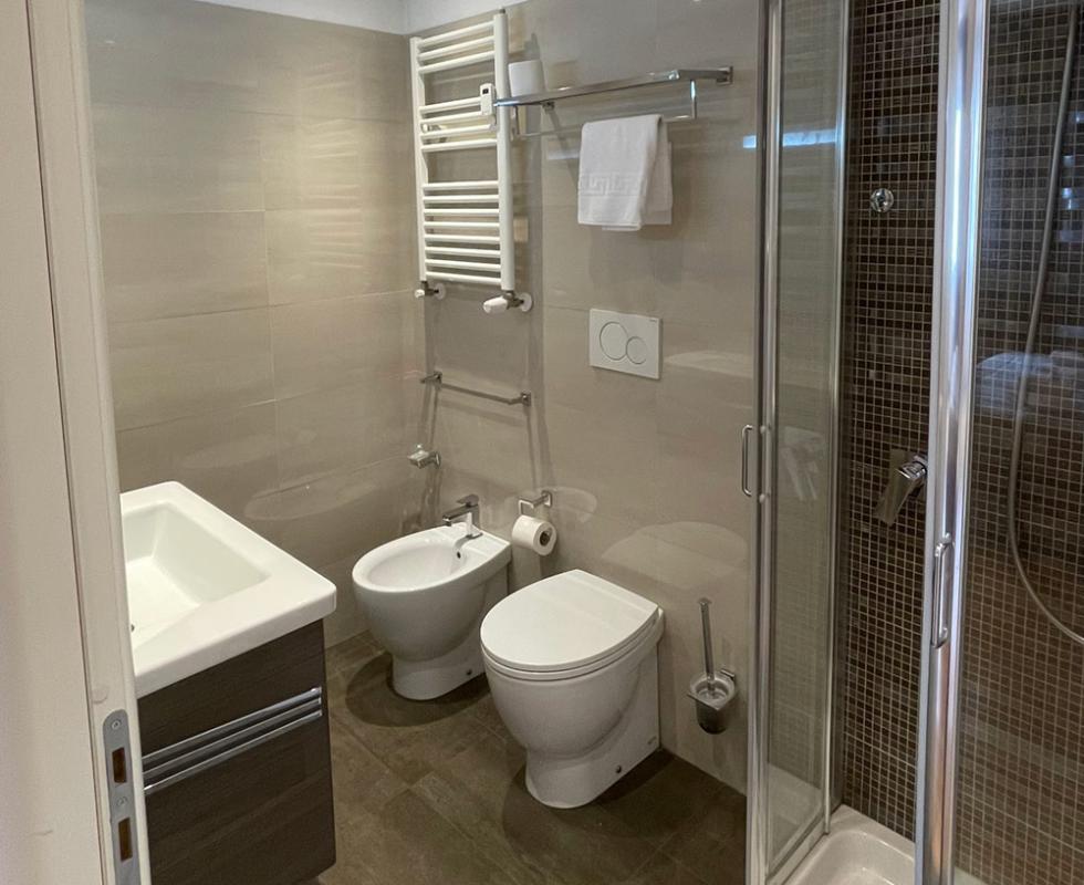 Bagno moderno con doccia, lavabo, bidet e WC, pavimento scuro e pareti chiare.